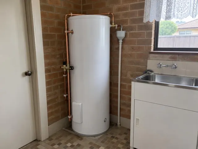 Newly installed hot water cylinder with copper pipework beside a sink in a brick laundry in Beresfield