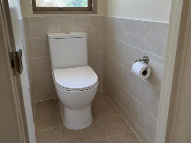 White toilet in a small tiled bathroom with a window and toilet roll holder in Tarro